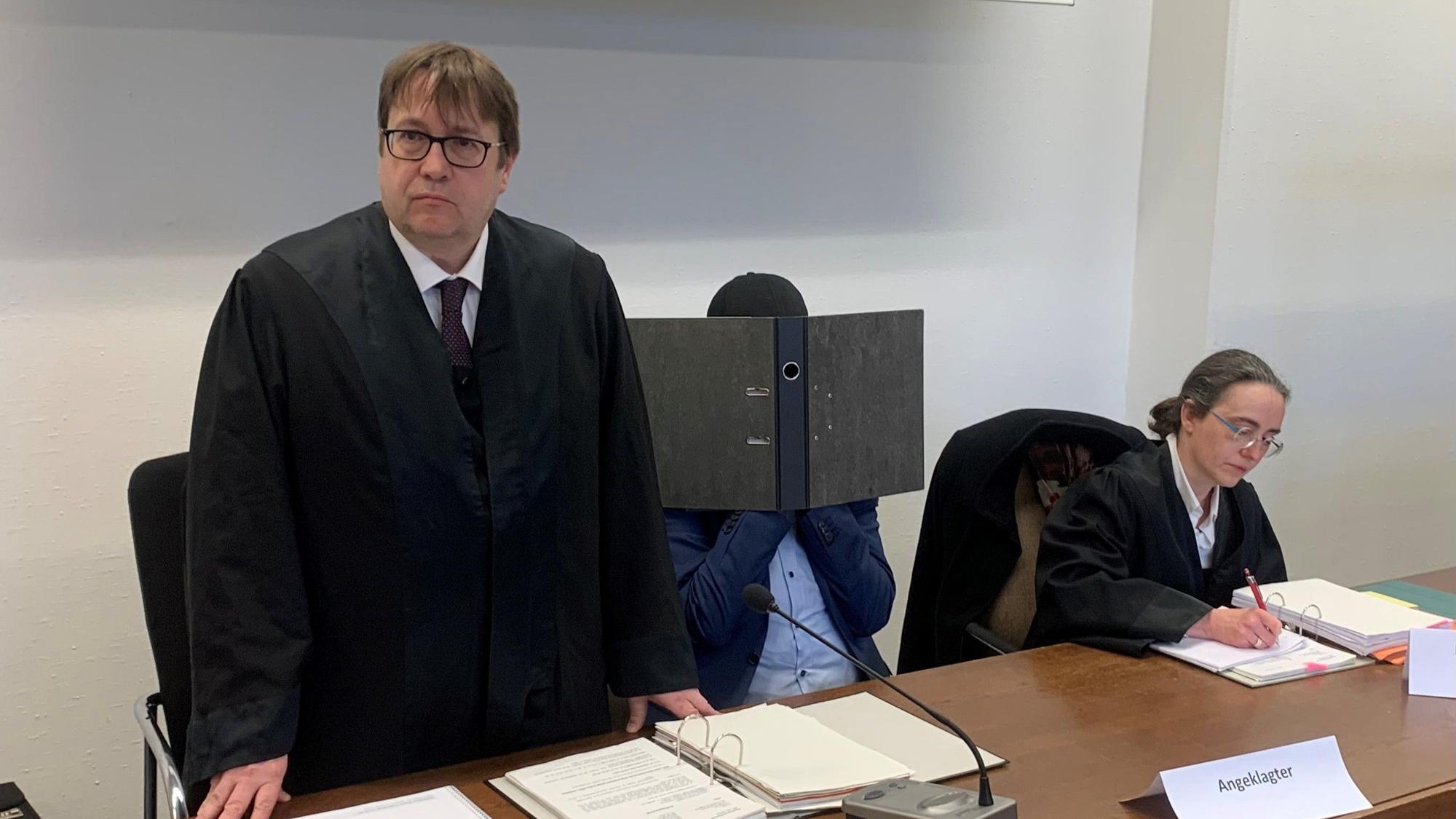 Der Angeklagte verbarg sein Gesicht mit einem Ordner vor den Fotografen im Saal.