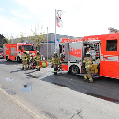 Feuerwehrfahrzeuge stehen auf einer gesperrten Straße. Feuerwehrleute laden Einsatzgerät aus.