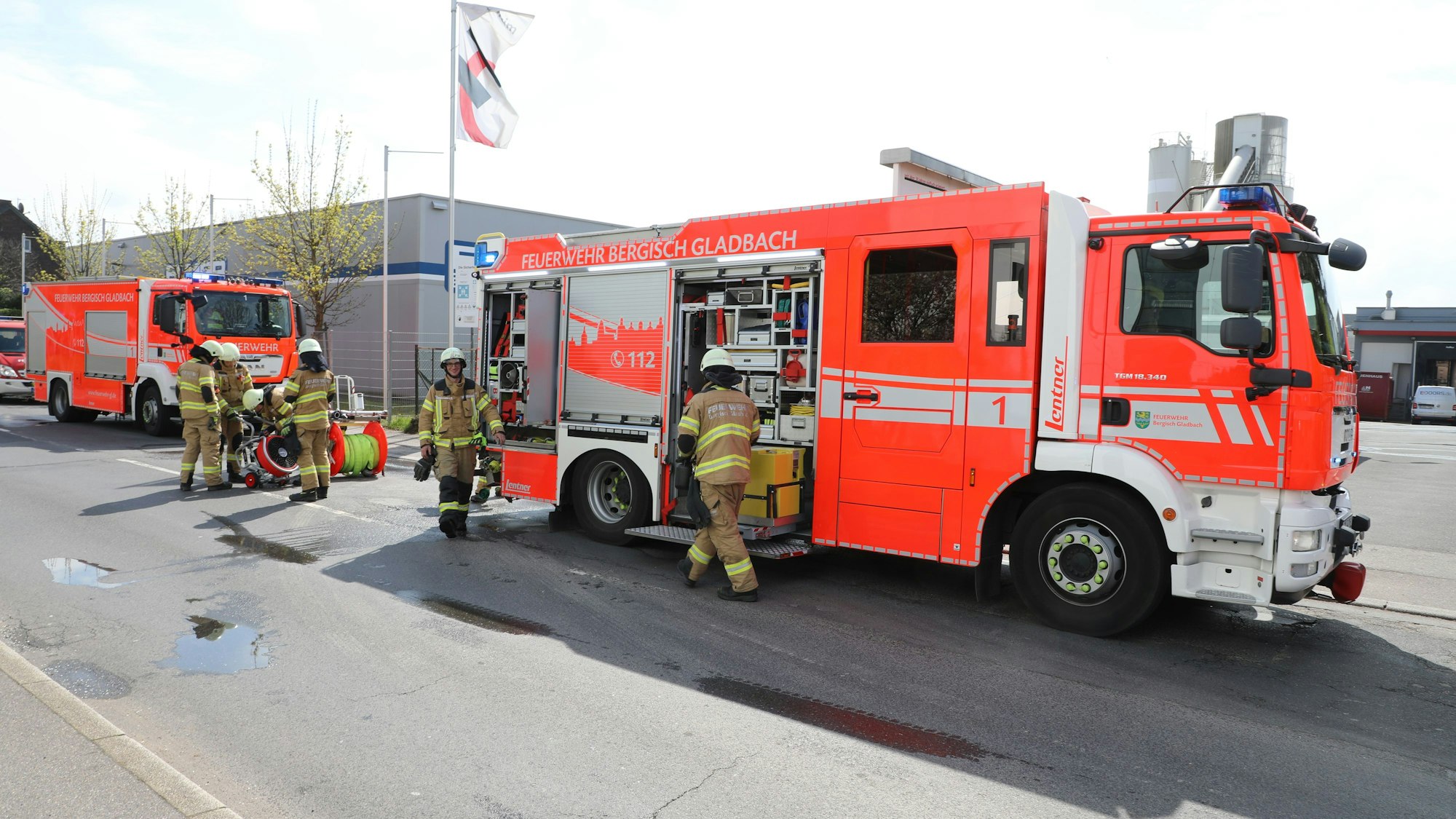 Feuerwehrfahrzeuge stehen auf einer gesperrten Straße. Feuerwehrleute laden Einsatzgerät aus.