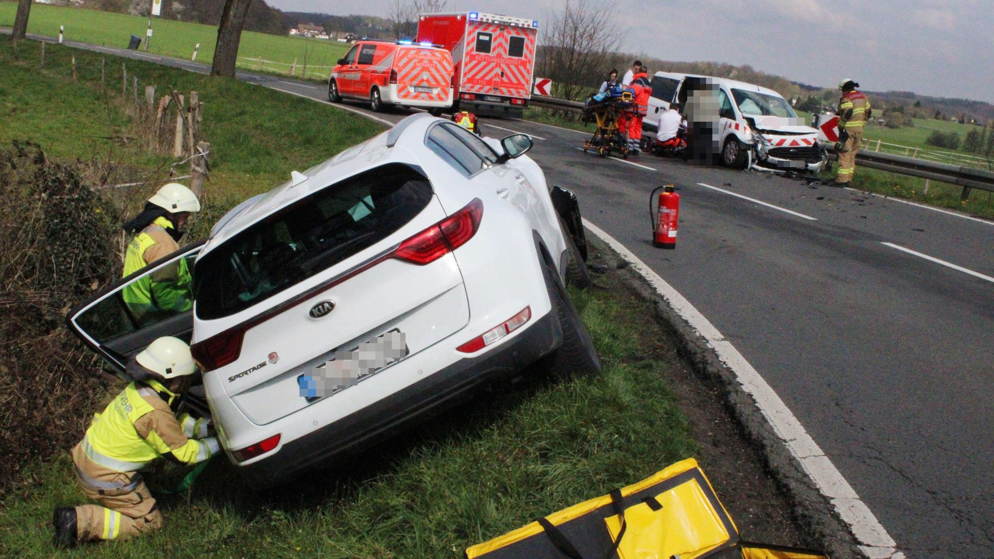 Schwer beschädigte Autos stehen neben einer Straße. Feuerwehrleute und Rettungsdienstmitarbeitende sind im Einsatz.