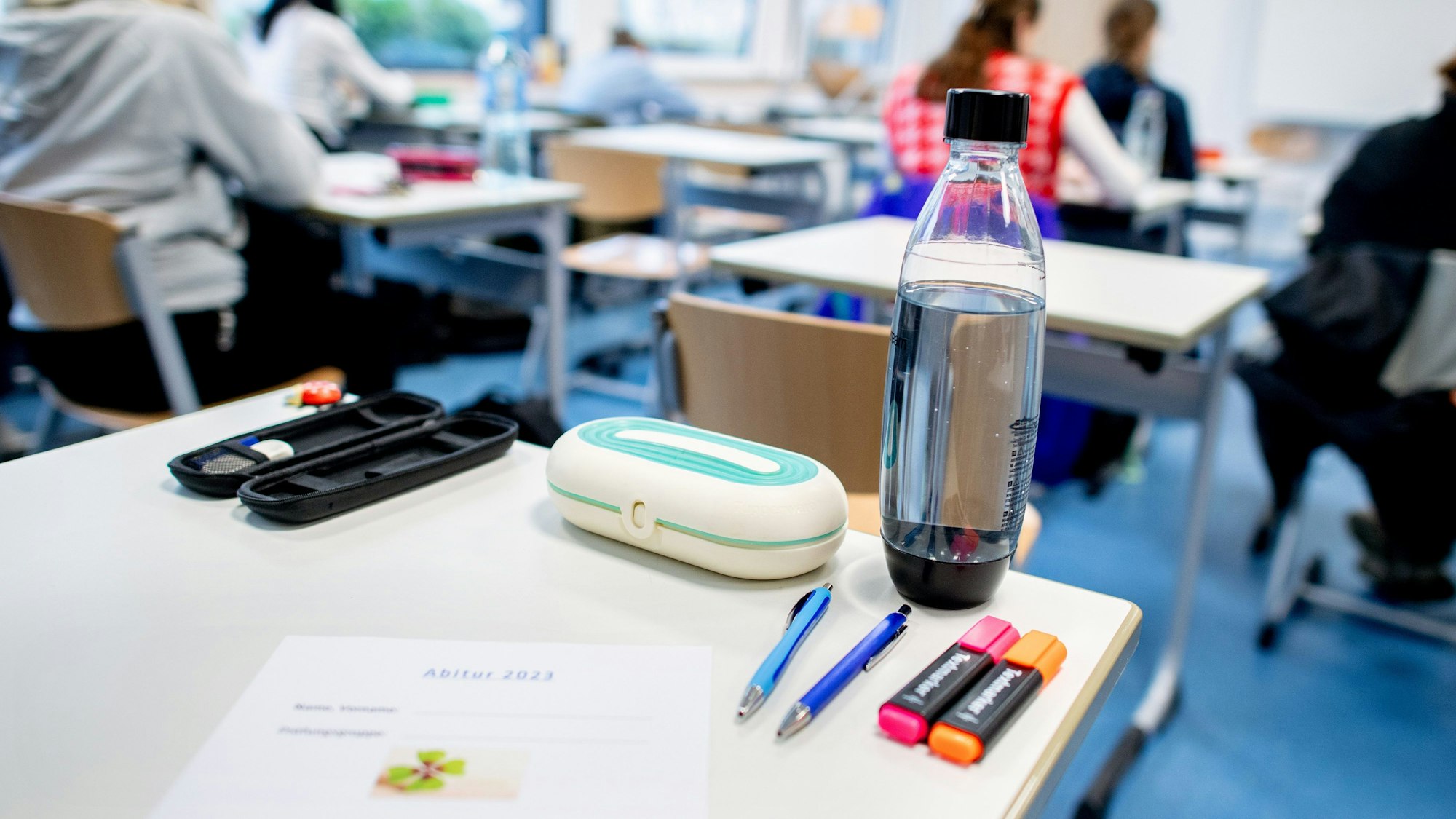 Mehrere Stifte liegen und eine Wasserflasche steht vor Beginn der schriftlichen Abiturprüfungen auf einem Tisch.