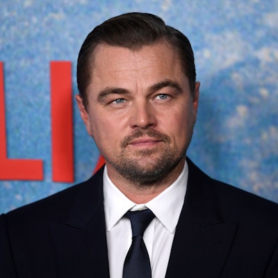Schauspieler Leonardo Di Caprio blickt auf dem Roten Teppich in die Kamera. Er trägt einen schwarzen Anzug.