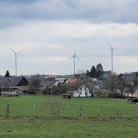 Im Vordergrund ein Dorf, dahinter stehen Windräder.