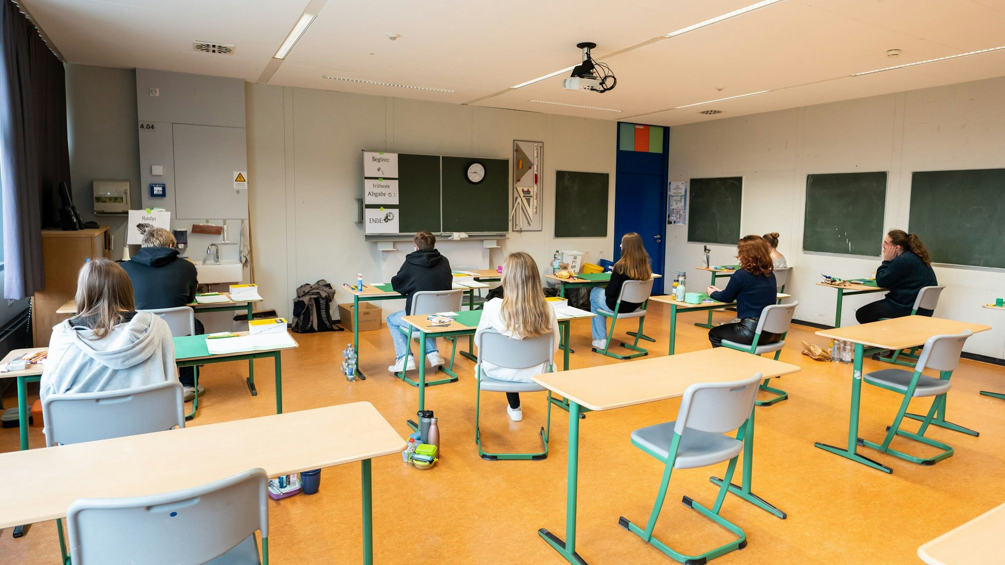Schülerinnen und Schüler sitzen vor Beginn der schriftlichen Abiturprüfung in Biologie in einem Klassenzimmer.