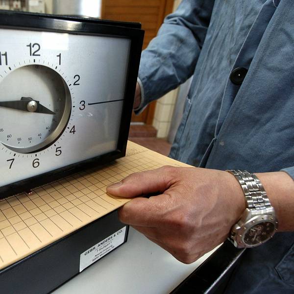 Eine Karte zur Arbeitszeiterfassung wird in einem Betrieb unter eine Stechuhr gelegt.