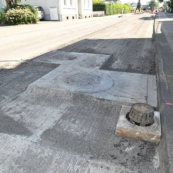 Eine gesperrte Straße ist abgefräst worden, die Kanaldeckel stehen über dem Straßenniveau.