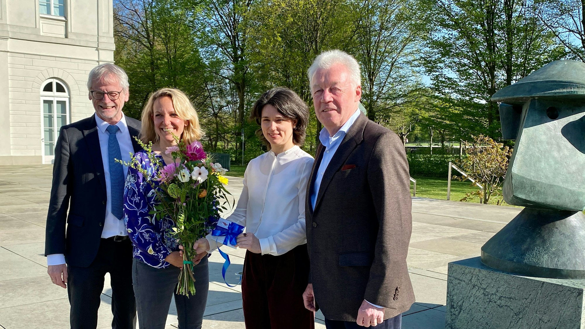 Die Museumsdirektorin überreicht der Kölnerin einen Strauß Blumen und eine Jahreskarte. Beide lächeln in die Kamera. Daneben stehen der Bürgermeister und Vorstandsvorsitzende.