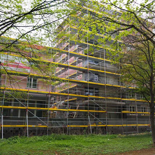 Ein von Baugerüsten umgebenes Gebäude mit rosa Fassade ist zu sehen.