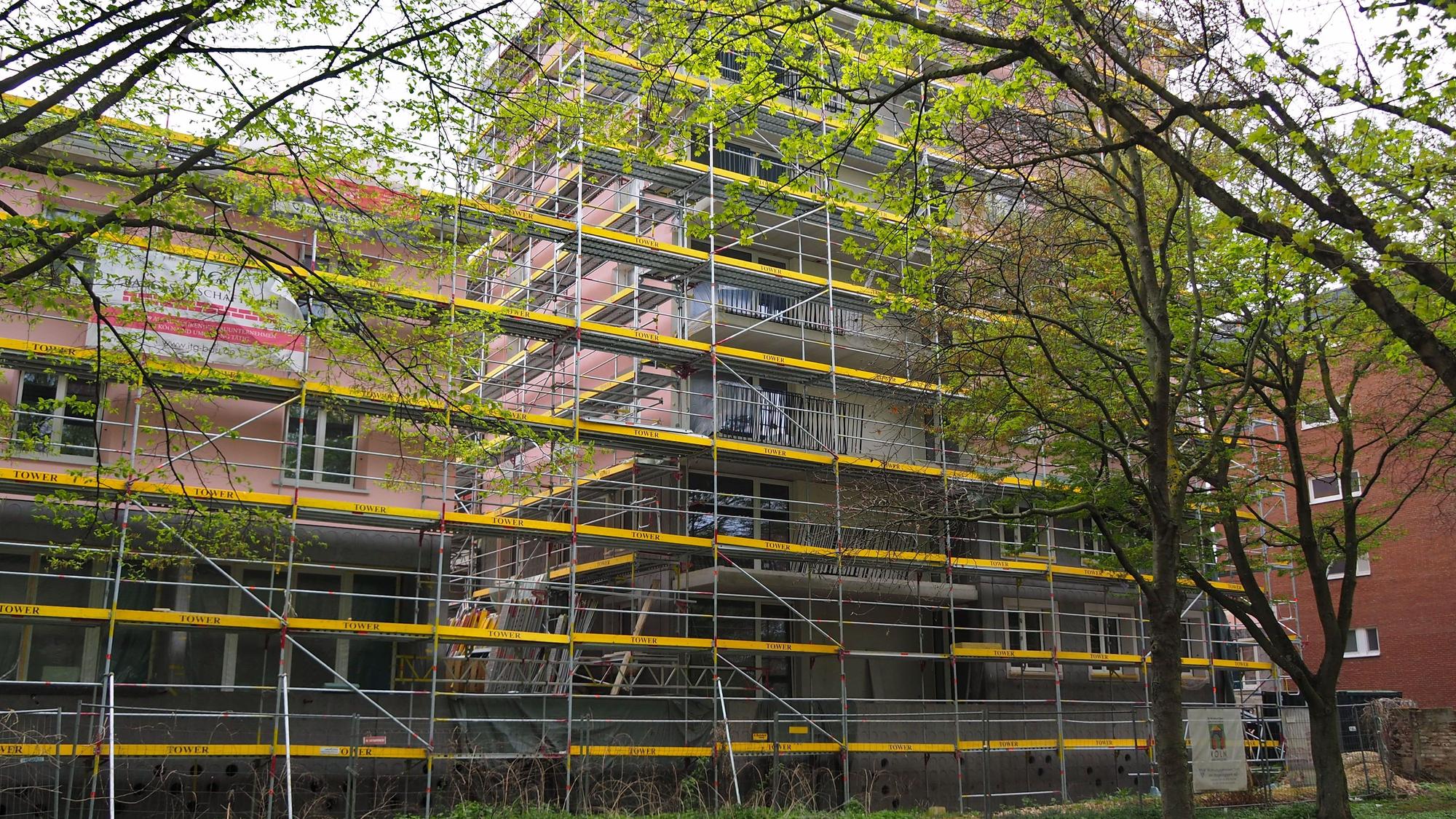 Ein von Baugerüsten umgebenes Gebäude mit rosa Fassade ist zu sehen.