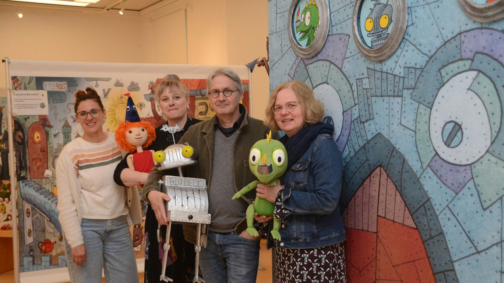 Drei Frauen und ein Mann stehen vor einem Bild, das Ritter Rost zeigt.