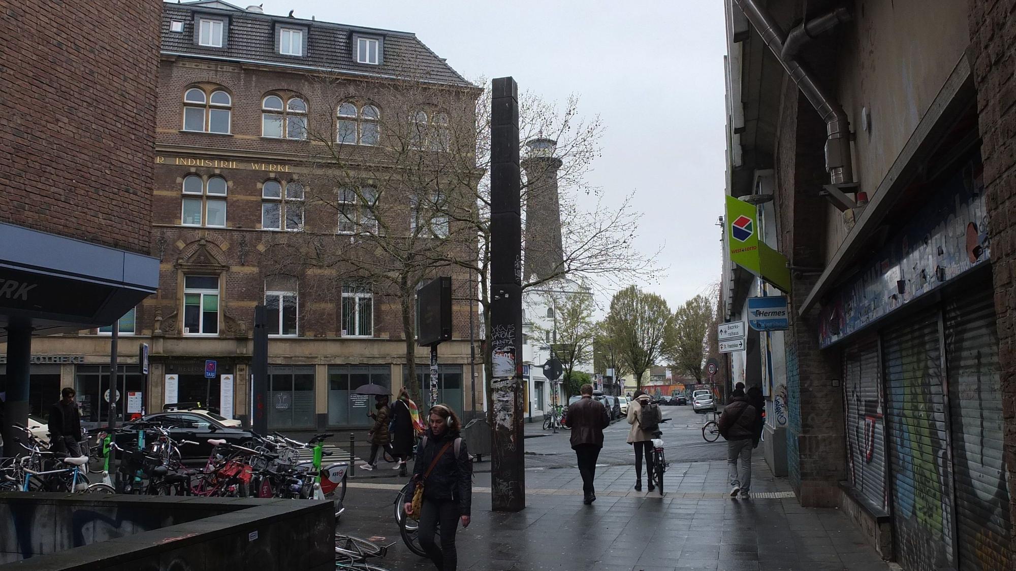 Die Stahlstele Streckung von Ansgar Nierhoff an der Venloer Straße umgeben von Häusern auf einem öffentlichen Platz.