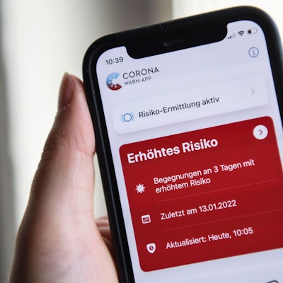 Eine Hand hält ein Smartphone, auf dem eine rote Warnmeldung der Corona-Warn-App zu sehen ist.