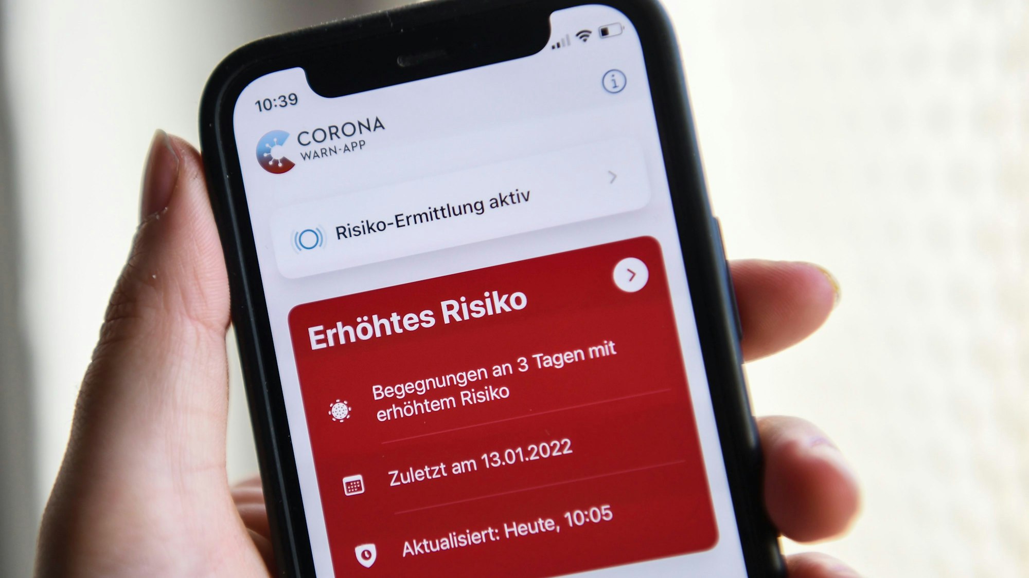 Eine Hand hält ein Smartphone, auf dem eine rote Warnmeldung der Corona-Warn-App zu sehen ist.