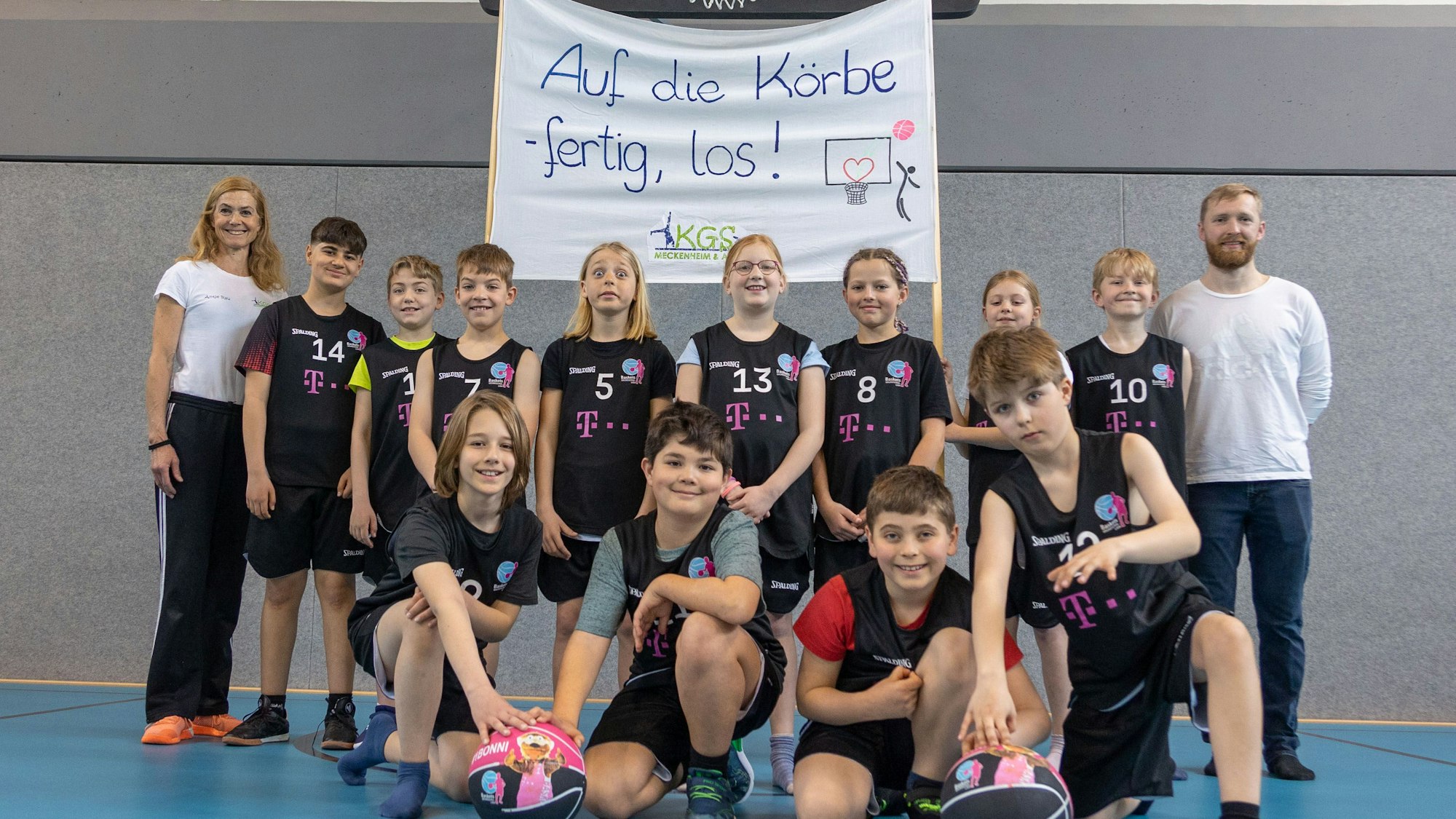 Die Sportlehrer Antje Rau und Daniel Miczka mit der Basketballmannschaft am 20.04.2023 bei der Vorstellung der neuen Trikots in der Katholischen Grundschule in Meckenheim. Foto Copyright: Petra Reuter