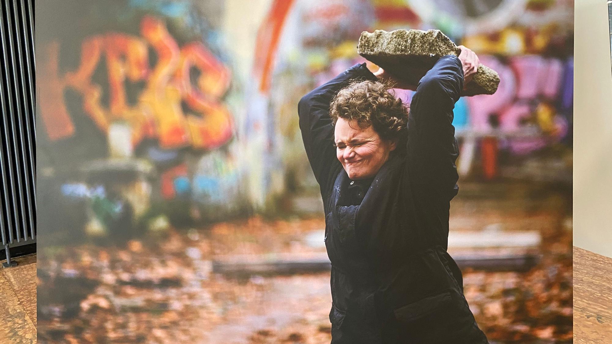 Eine Fotoleinwand zeigt eine Frau, die einen großen Stein schmeißt.
