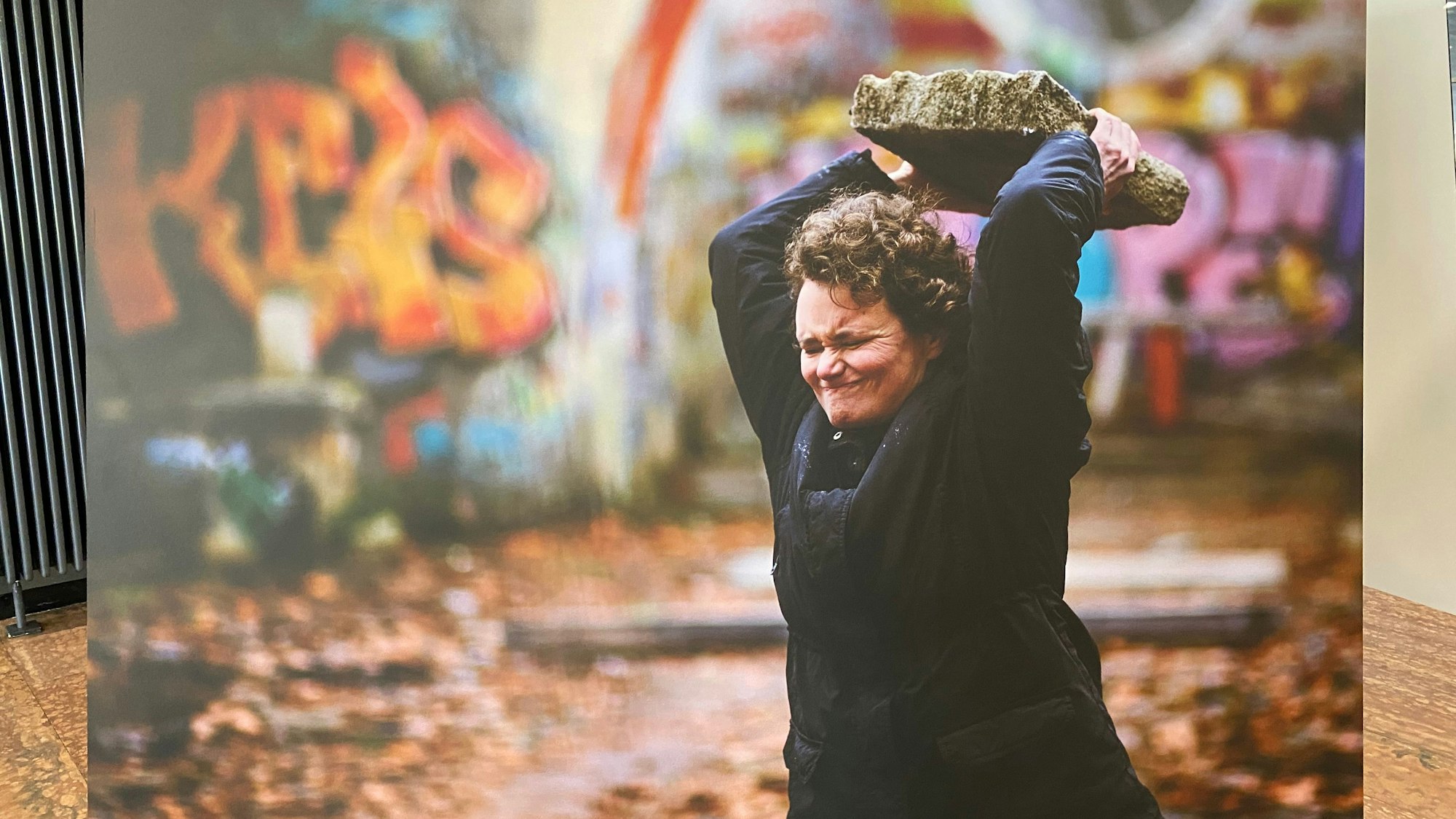 Eine Fotoleinwand zeigt eine Frau, die einen großen Stein schmeißt.