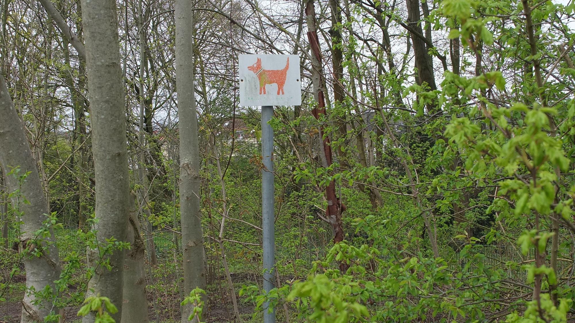 Ein Schild, auf dem ein Hund abgebildet ist inmitten von Bäumen und Gebüschen.