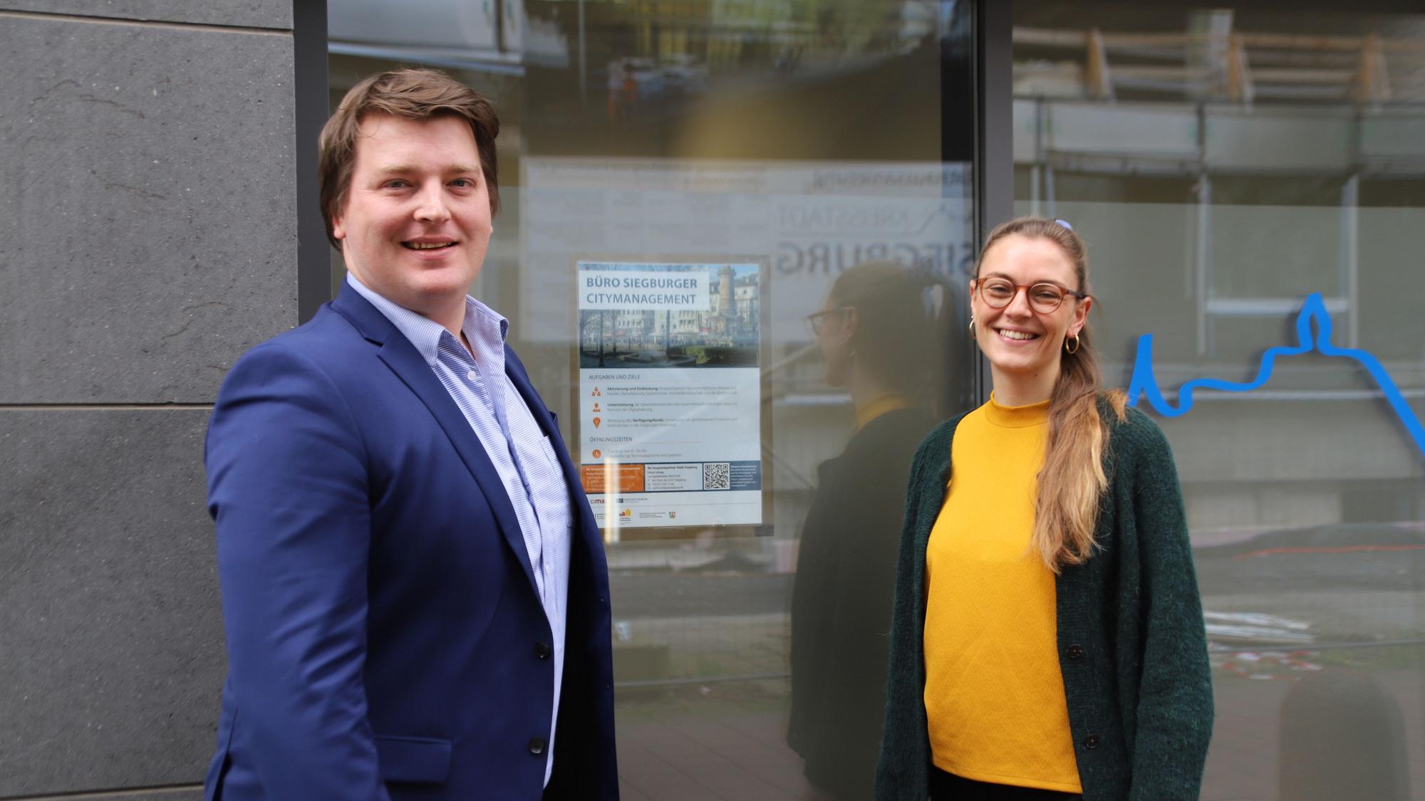 Helge Harnack (l.) und Amelie Strigl stehen vor der Tür zu ihrem Büro und lächeln in die Kamera.