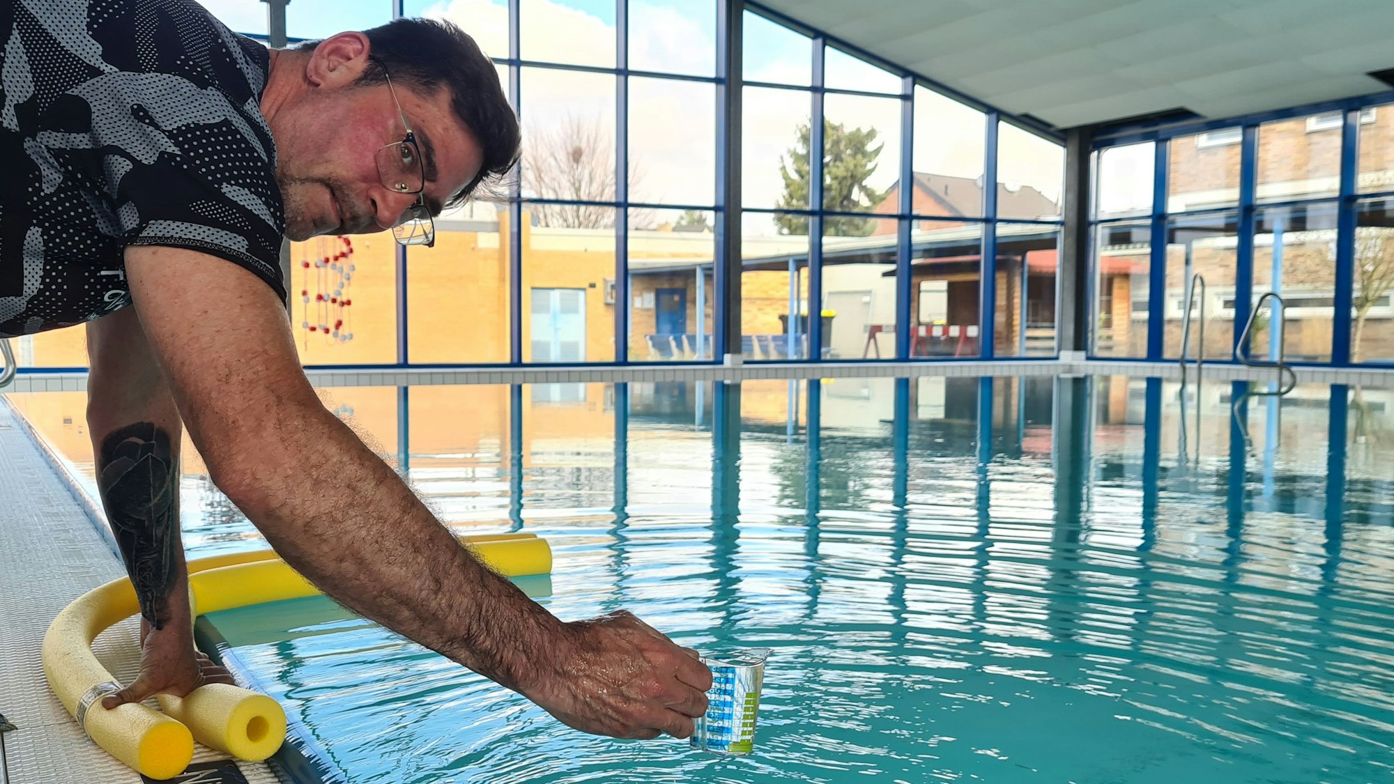 Das Bild zeigt einen Mann, der im Schwimmbad einen Wasserprobe nimmt.