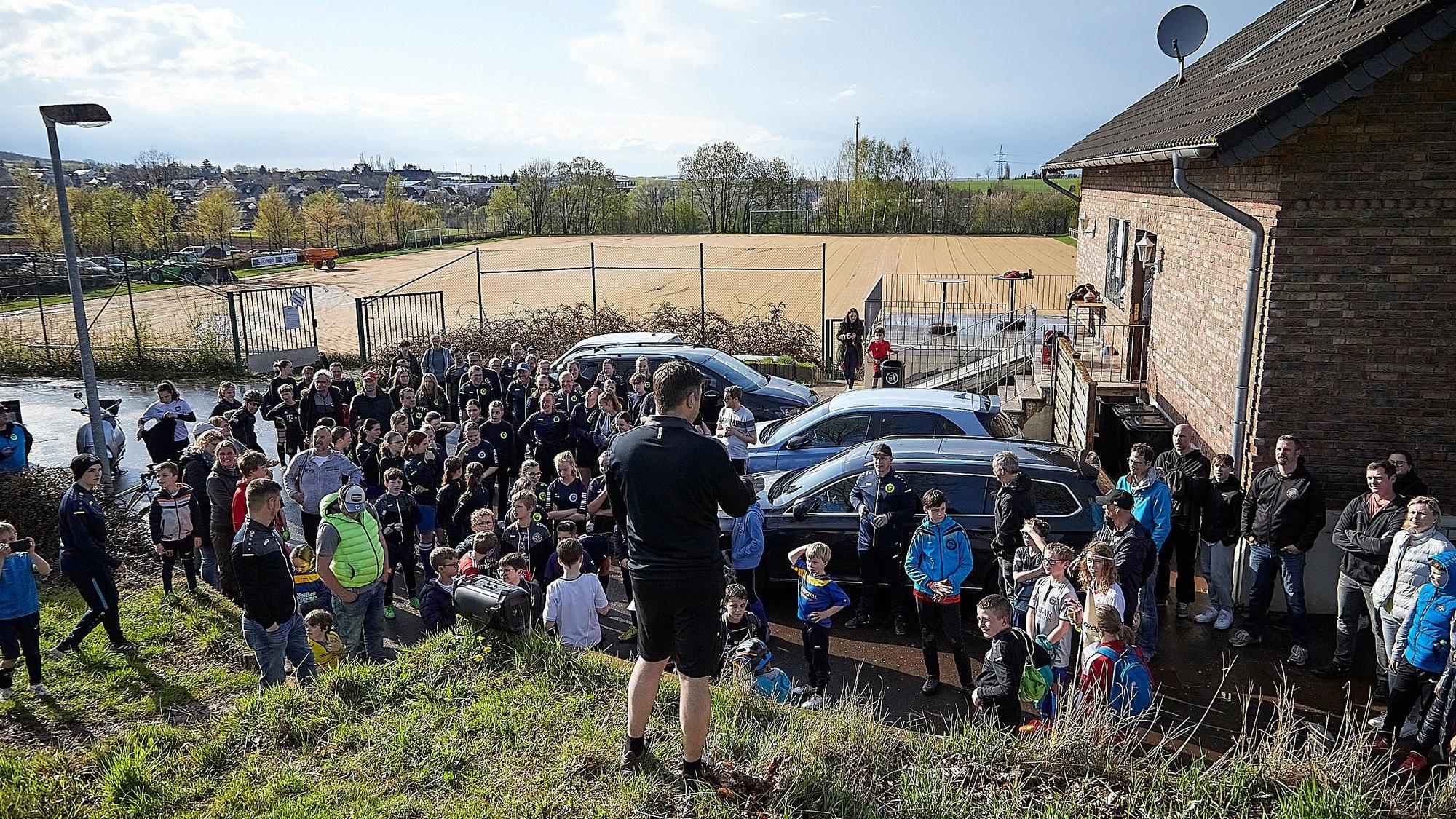 Während rund 100 Vereinsmitglieder einem Vertreter des Vorstands zuhören, sieht man im Hintergrund die Sandfläche des abgetragenen Rasenplatzes.