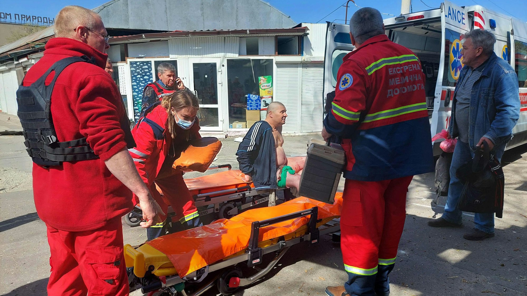 EDITORS NOTE: Graphic content / A wounded man is treated by medics at a market in the center of the Ukrainian city of Kherson following a Russian shelling, on April 18, 2023. - After Putin's visit was made public on Tuesday, Ukrainian officials said Russian forces had shelled the center of Kherson, killing one and injuring nine. (Photo by Dina Pletenchuk / AFP)