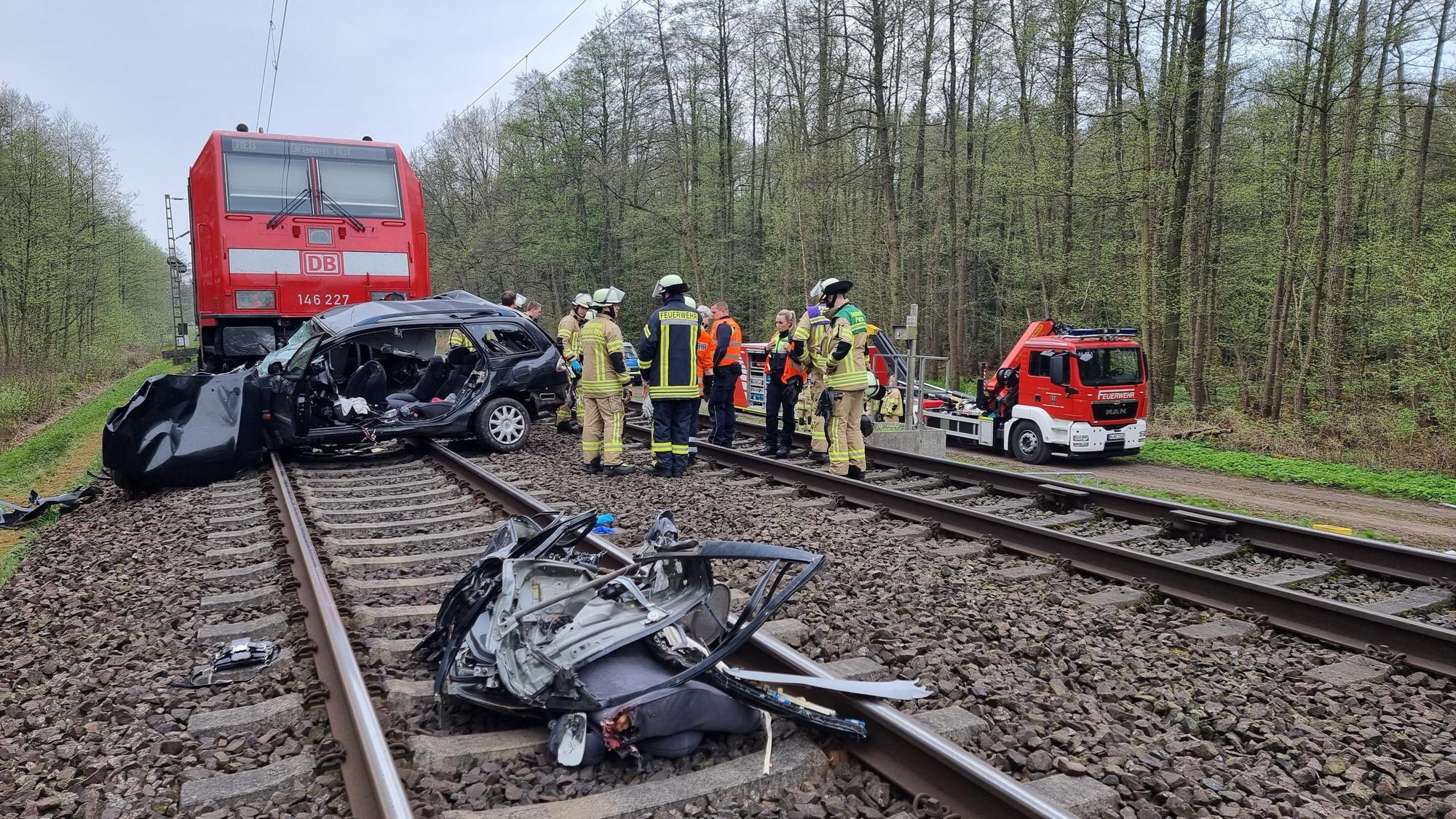 Ein Autowrack liegt auf den Gleisen, dahinter ist ein Zug zu sehen. Einsatzkräfte stehen an den Gleisen und unterhalten sich.