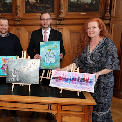Menschen stehen mit Bildern auf kleinen Staffeleien um einen Tisch im Bergisch Gladbacher Ratssaal.