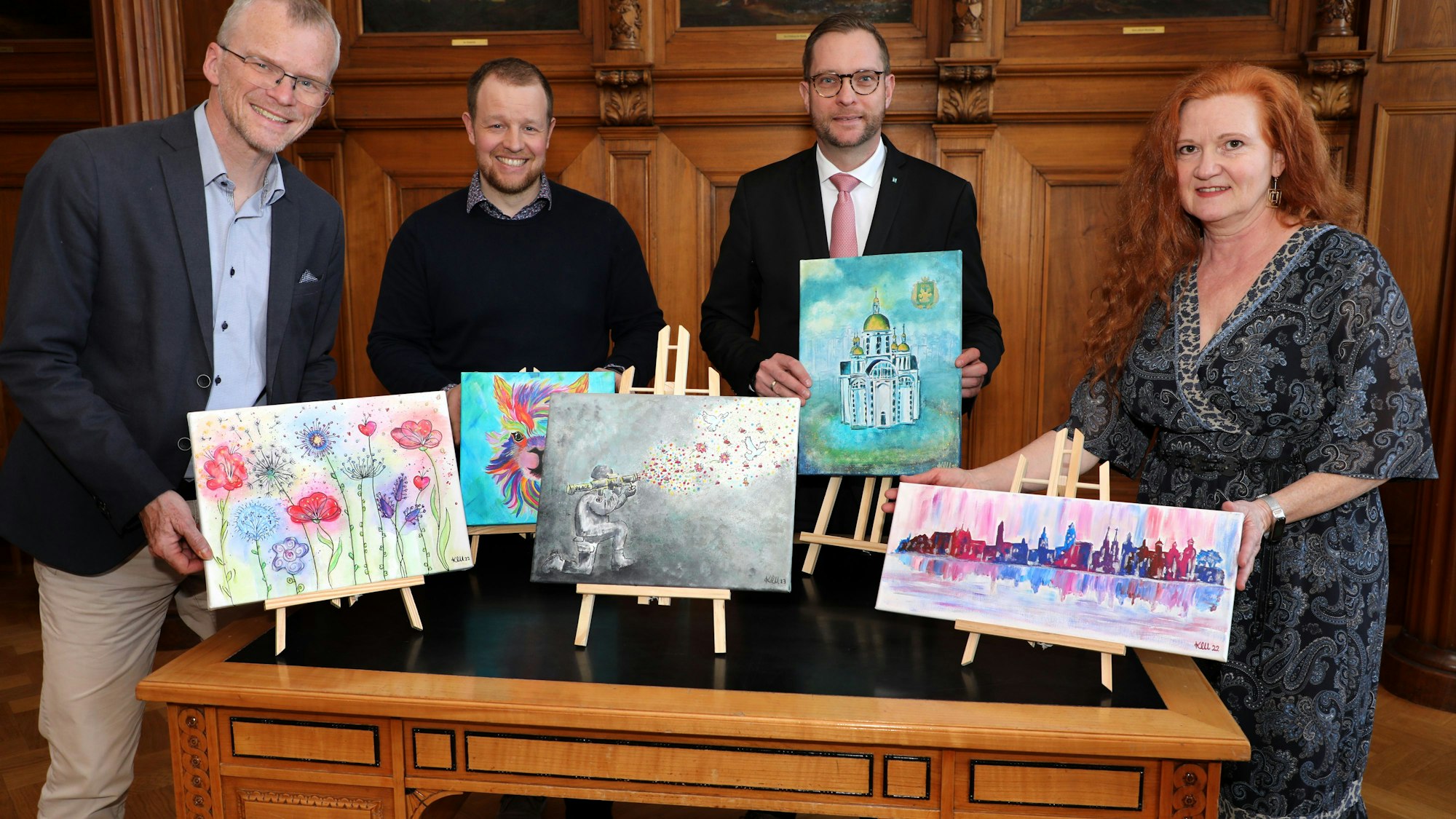 Menschen stehen mit Bildern auf kleinen Staffeleien um einen Tisch im Bergisch Gladbacher Ratssaal.
