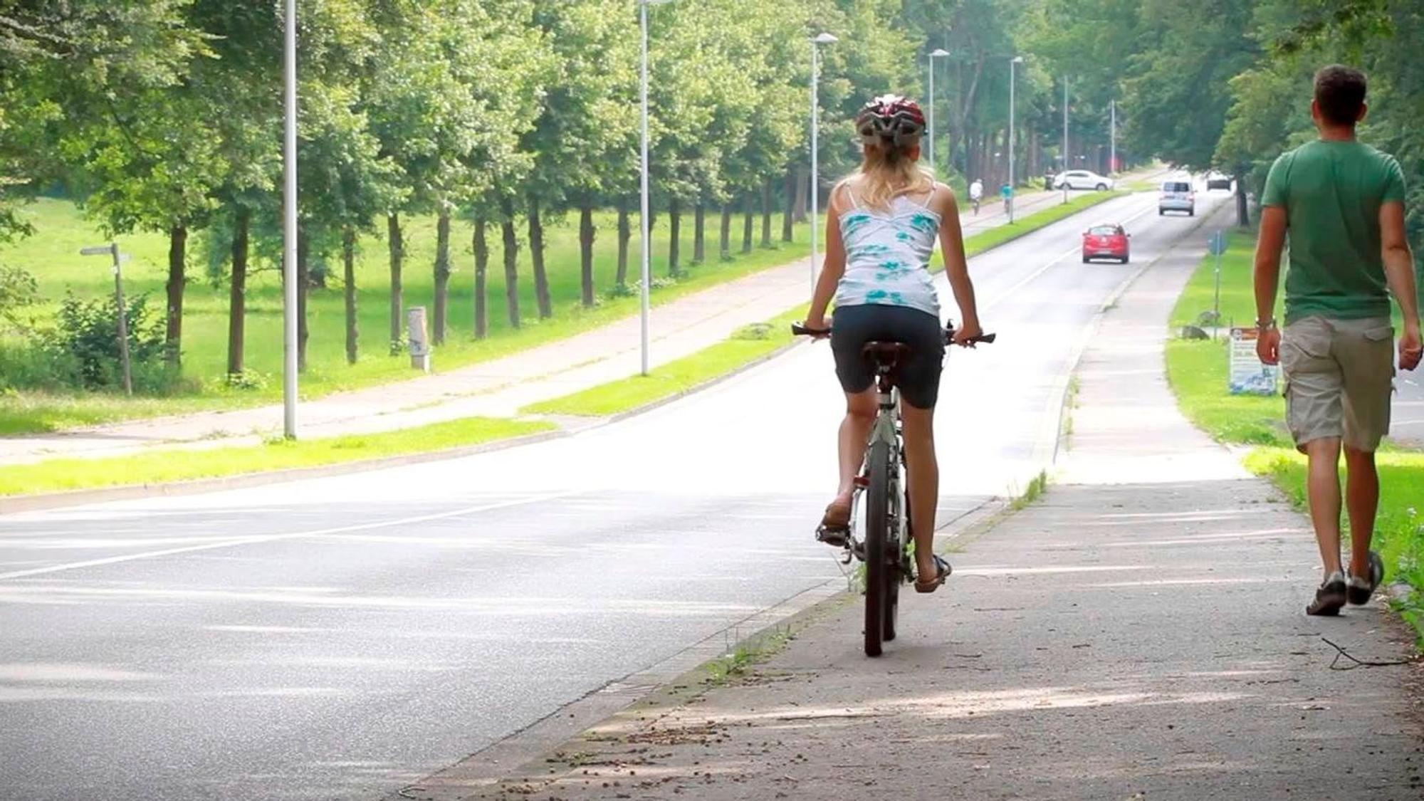 Mit dem Rad sicher durch den Straßenverkehr. Eine Radfahrerin und ein Fußgänger zeigen wie Konflikte vermieden werden können