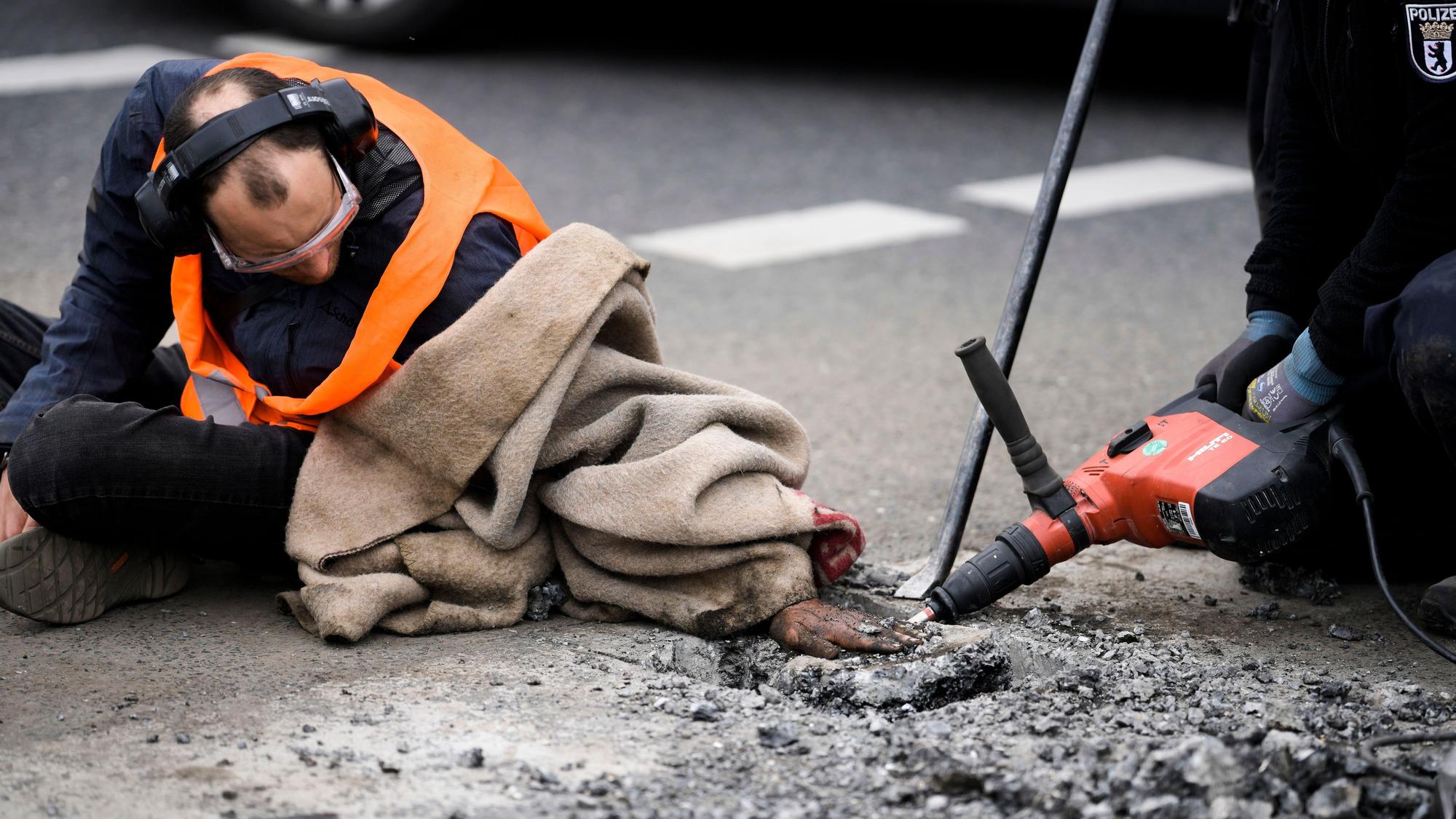 Die Polizei entfernt den Asphalt neben der Hand eines Klimaaktivisten, der seine Hand auf die Straße geklebt hat, während einer Demonstration gegen die Klimapolitik der deutschen Regierung in Berlin.