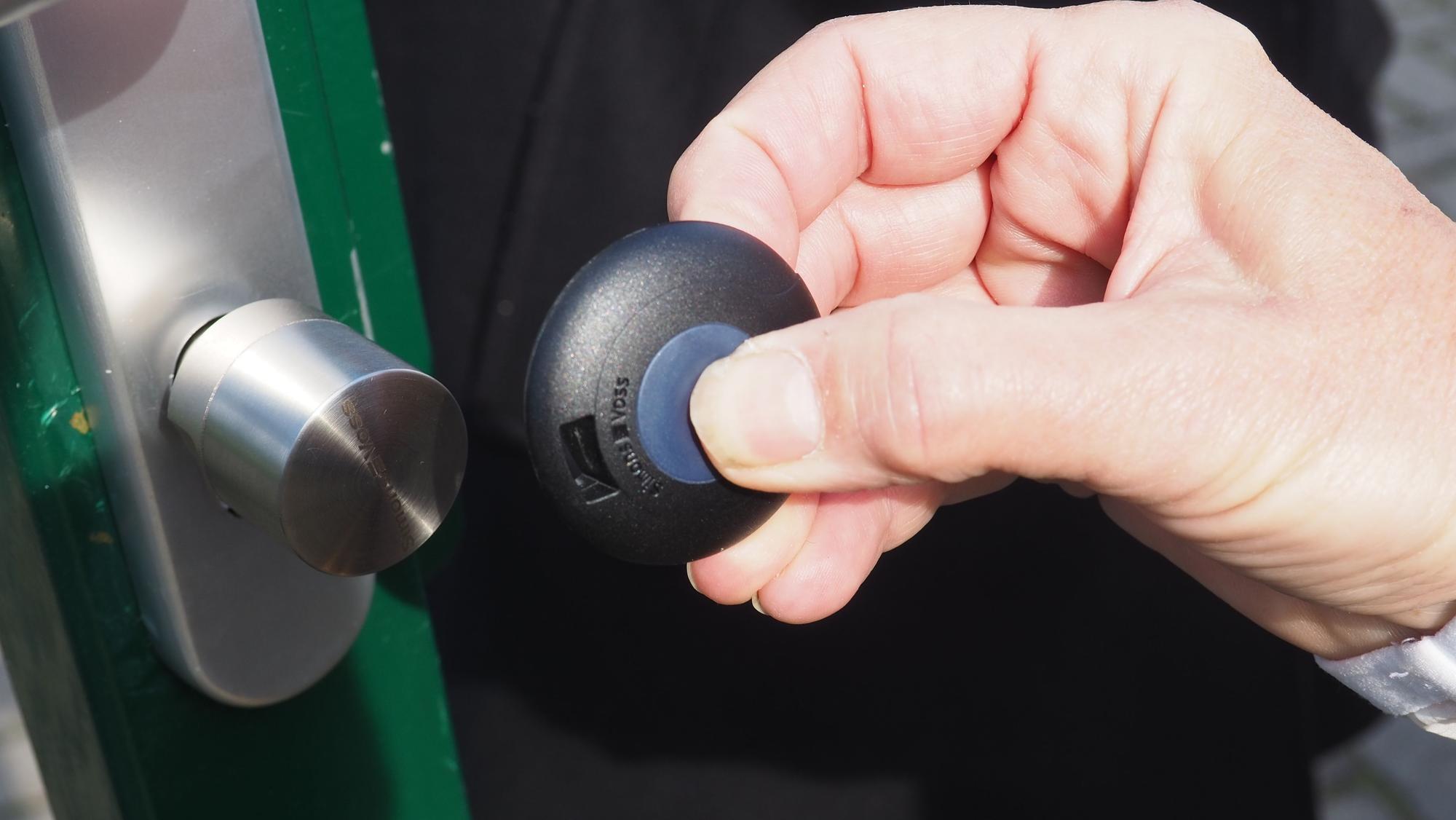 Eine Hand hält einen Transponder an ein elektrisches Türschloss.