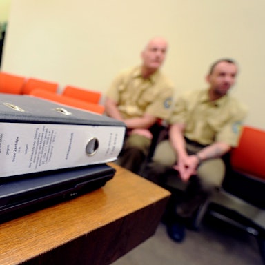 Eine Akte zum NSU-Prozess liegt im Gerichtssaal in München, (Bayern) während zwei Polizisten auf einer Bank sitzen. (Symbolbild)