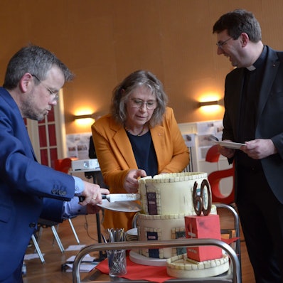 Die Vorstände Martin Jost (v.l.) und Maria Surges-Brilon schneiden die Geburtstagstorte an, Kreisdechant Guido Zimmermann assistiert.