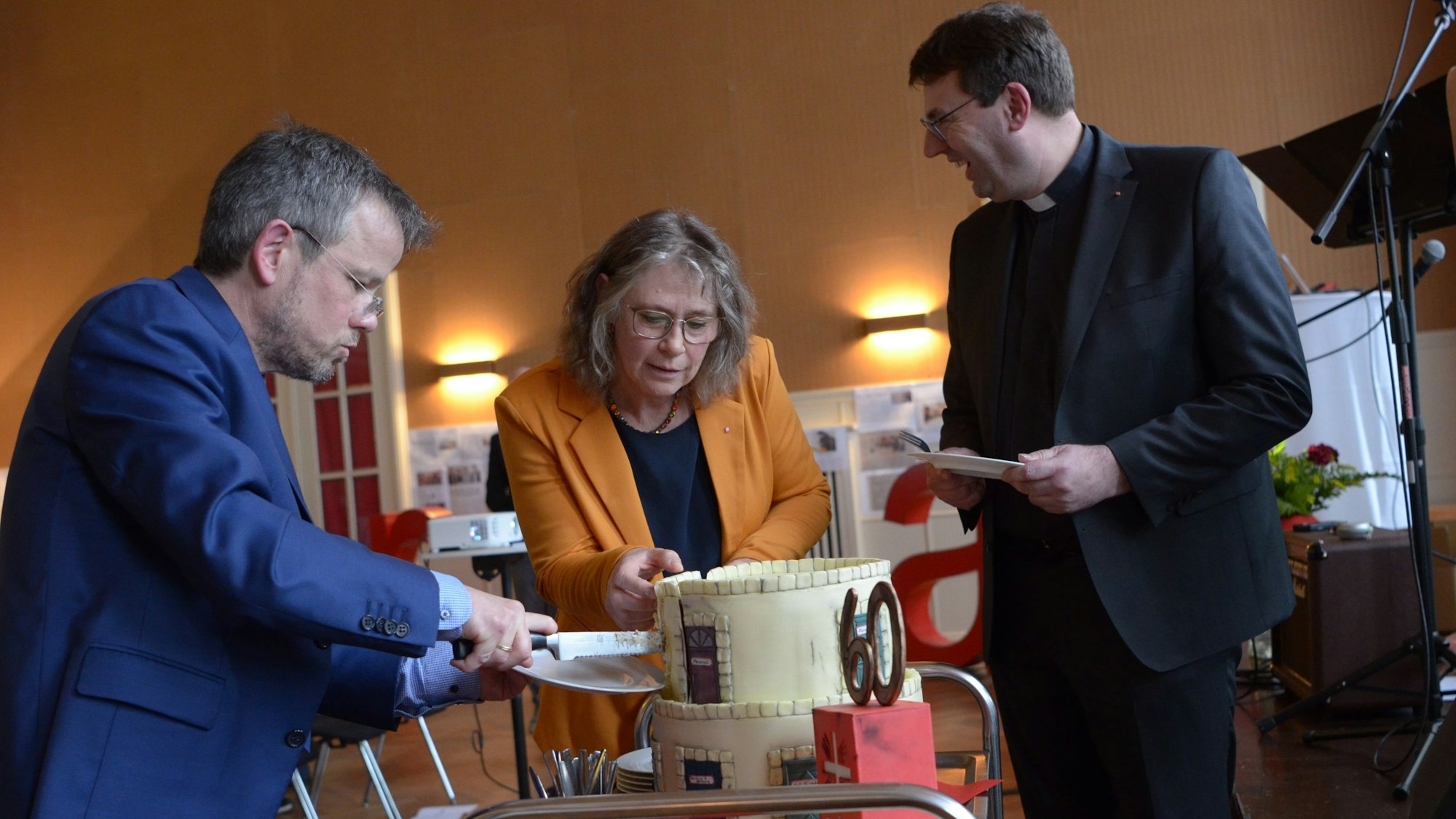 Die Vorstände Martin Jost (v.l.) und Maria Surges-Brilon schneiden die Geburtstagstorte an, Kreisdechant Guido Zimmermann assistiert.