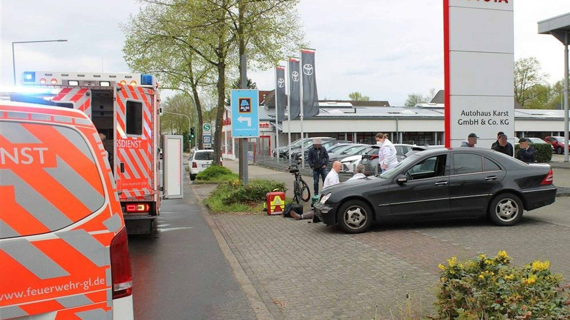 Ein Auto steht an der Ausfahrt eines Autohauses. Daneben behandeln Sanitäter eine liegende Person.