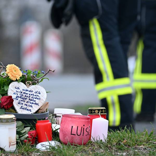 Kerzen und Blumen liegen an einem Baum an der Gesamtschule der getöteten Luise (12) in Freudenberg. Im Hintergrund ist ein Polizist zu sehen.