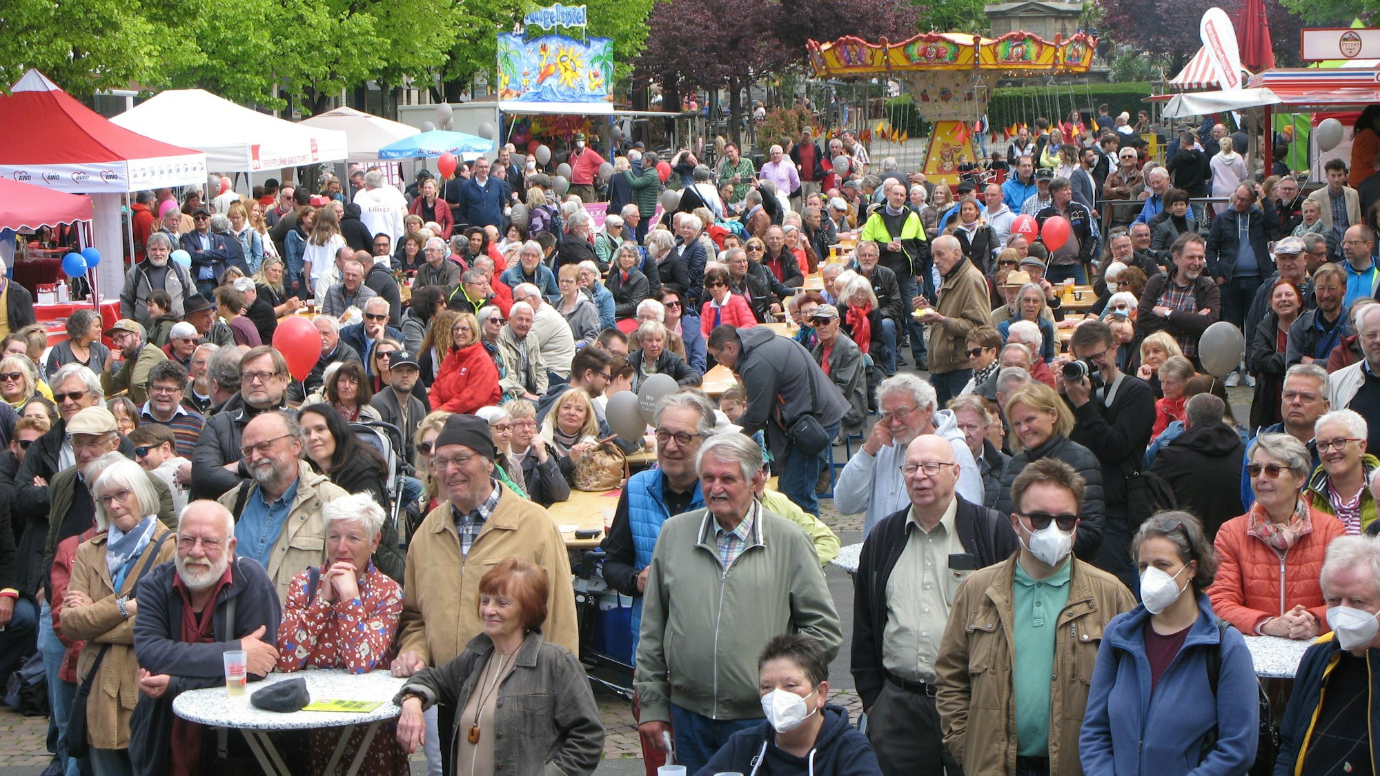 Eine größere Menschenmenge steht auf dem Siegburger Marktplatz. Einige Personen tragen Masken, die meisten aber nicht. Im Hintergrund stehen Fahrgeschäfte.