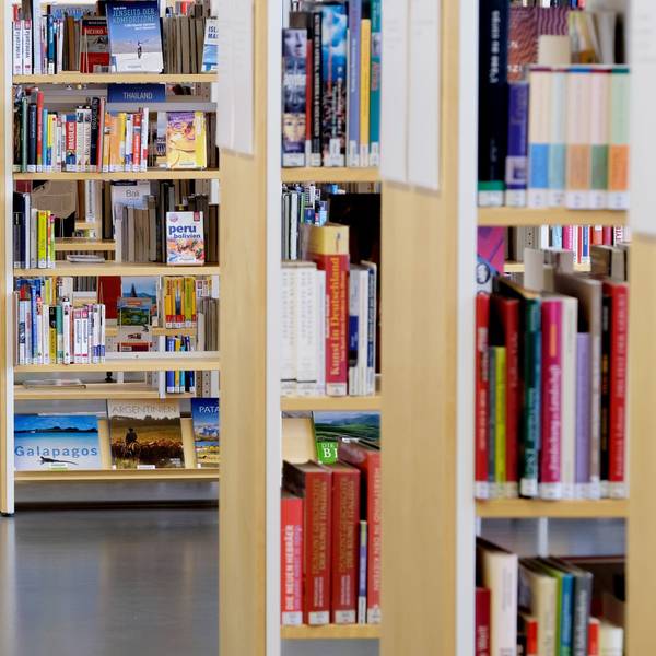 Eine Mitarbeiterin geht an Bücherregalen vorbei. (Symbolbild)