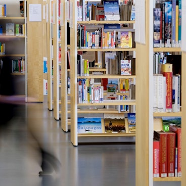 Eine Mitarbeiterin geht an Bücherregalen vorbei. (Symbolbild)