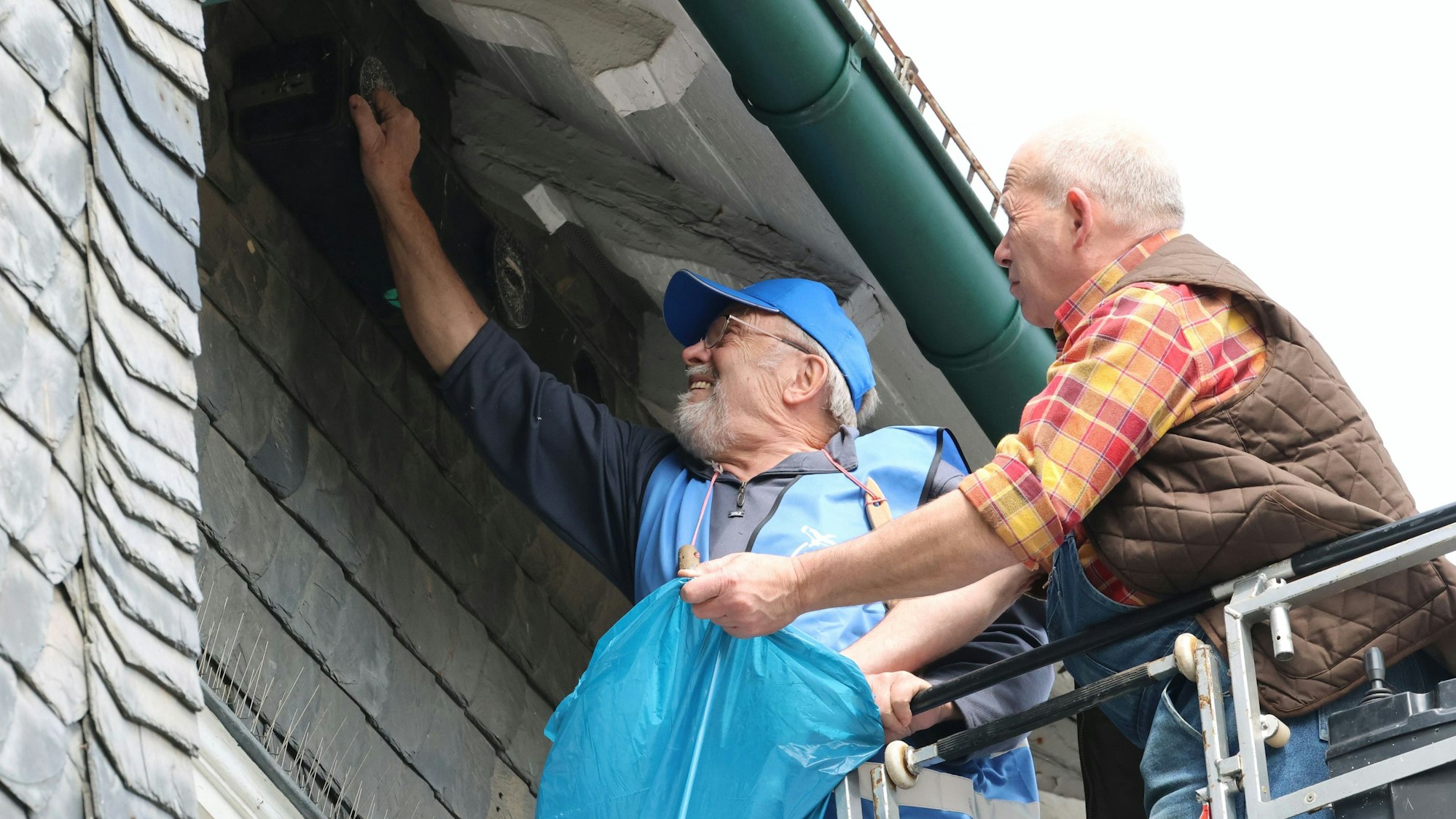 Hans Krämer und Joachim Müsse stehen im Korb der Drehleiter und reinigen einen Mauersegler-Nistkasten.