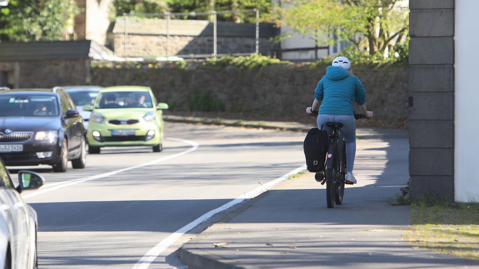 Ein Radfahrer fährt in Höhe des Klosters Heisterbach auf dem kombinierten Fuß-Fahrrad-Weg bergauf, auf der Landesstraße 268 links daneben fahren mehrere Autos bergab.