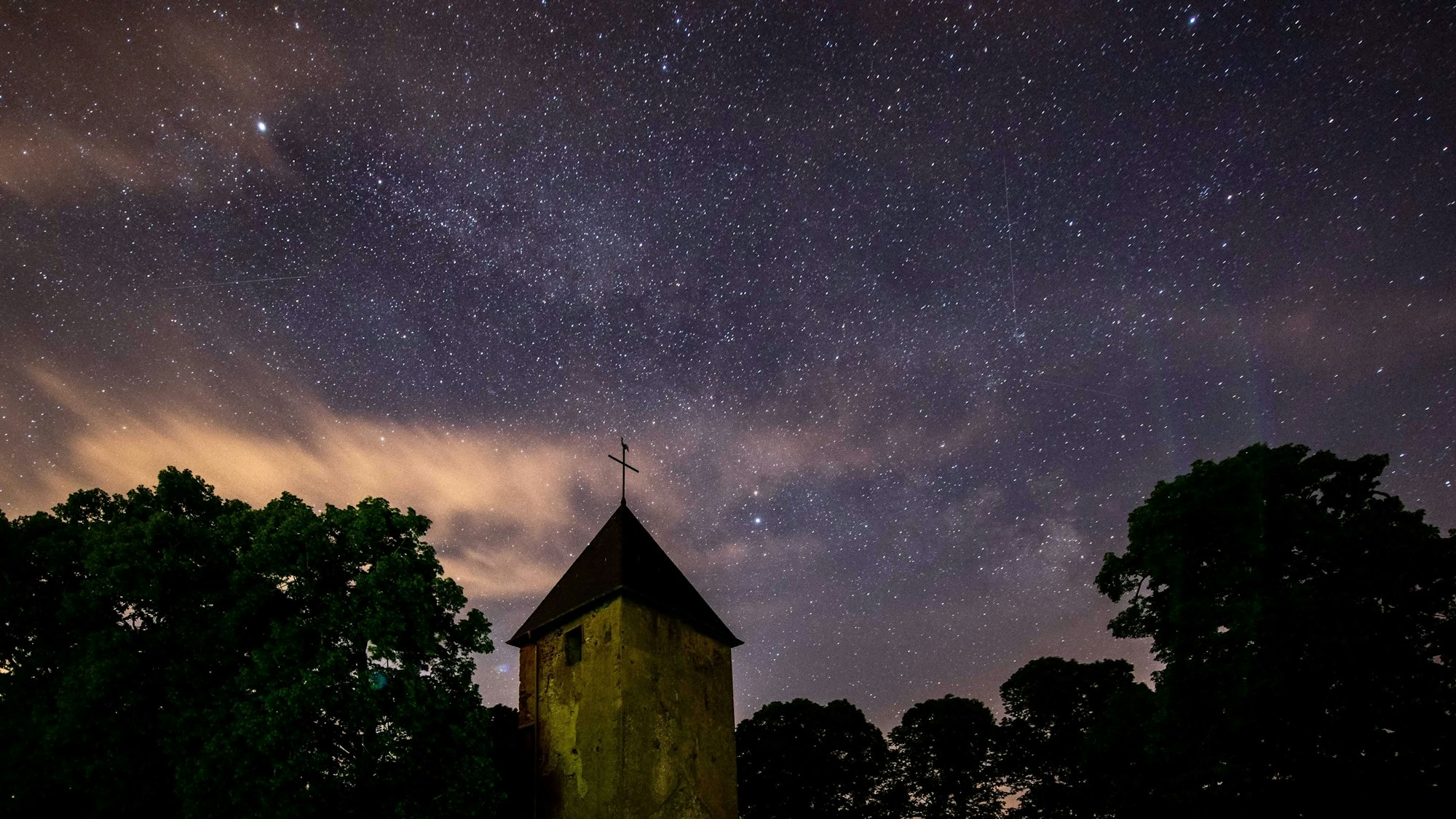 Der Wollseifener Kirchturm und einige Baumkronen ragen in den Sternenhimmel.
