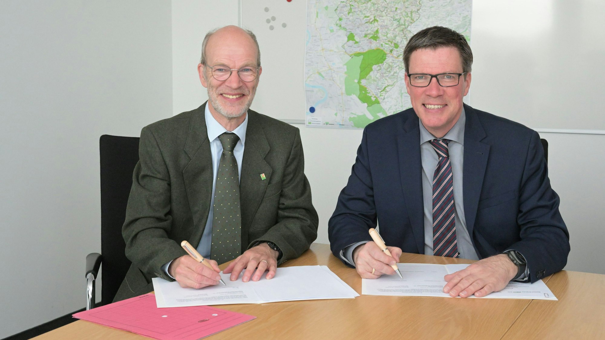 Zwei Menschen sitzen an einem Tisch und unterschreiben Verträge.