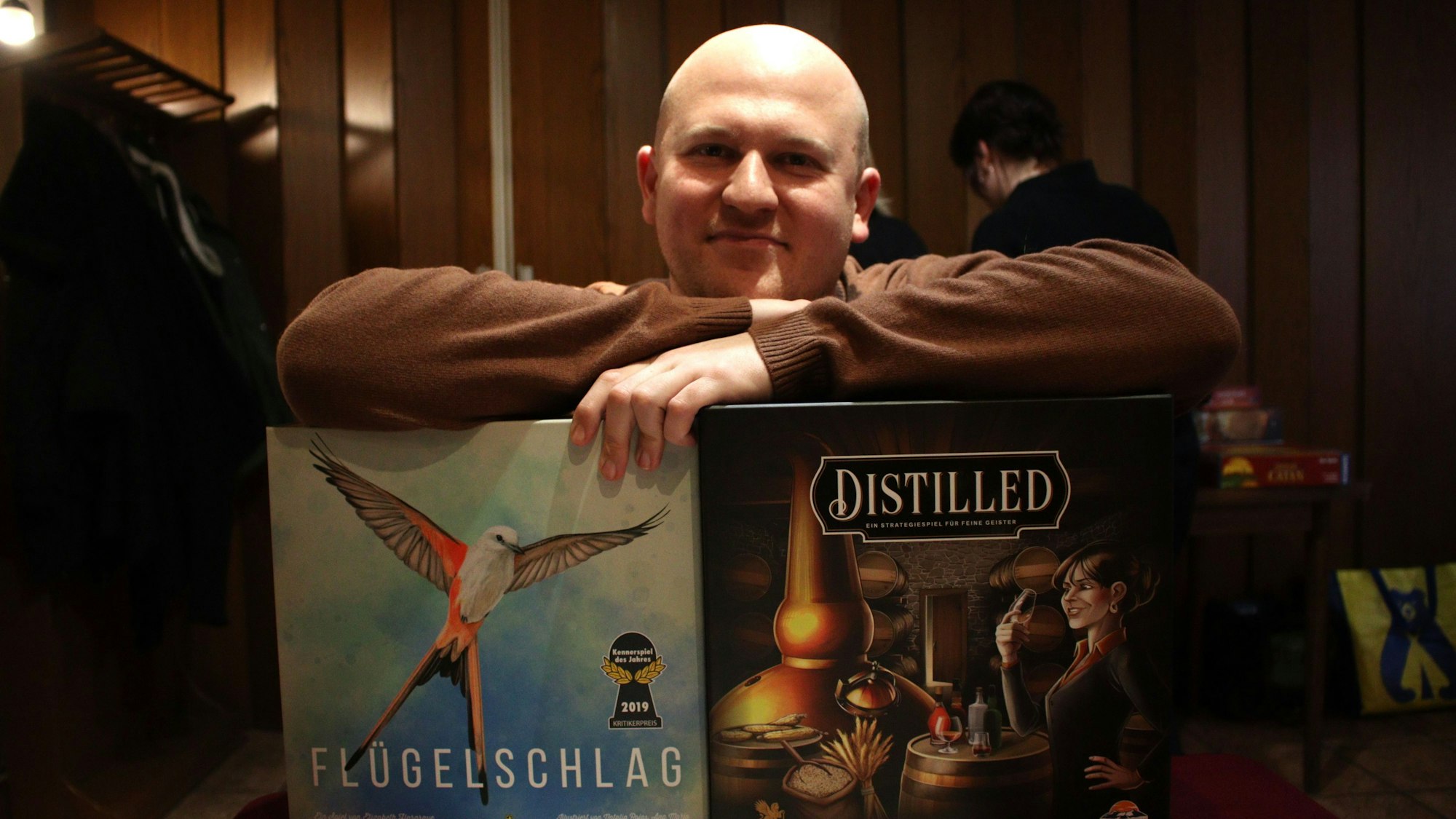 Gründer Martin Finder lehnt sich auf die Umverpackung zweier Brettspiele.