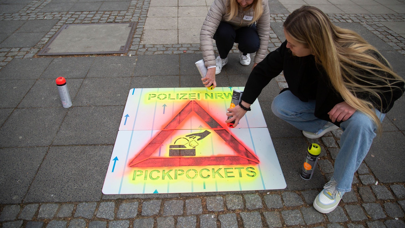 Mit Sprühkreide bringen Polizistinnen am Neumarkt in Köln Warnungen vor Taschendieben an.