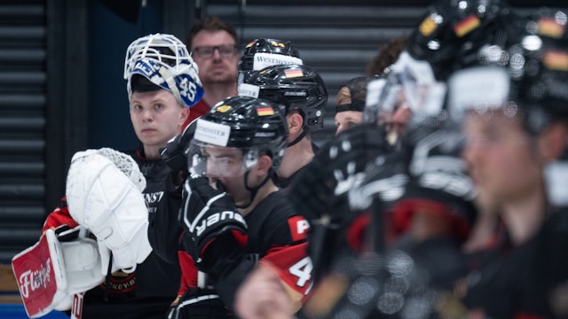 Eishockeyspieler stehen unscharf vor einem Torwart.