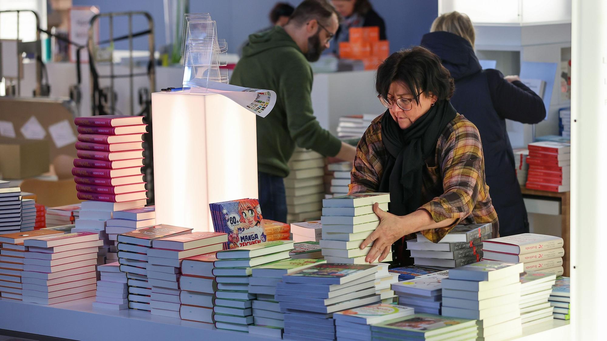 Eine Frau stapelt Bücher auf einem Tisch.