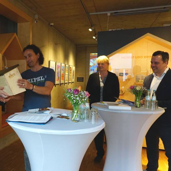 Landrat Markus Ramers überreicht Stefan Brings, dem Paten der Aktion „Zu Gast in der eigenen Heimat“ ein „Hummelhaus“. Um sie herum drei weitere Personen. Sie befinden sich drinnen.