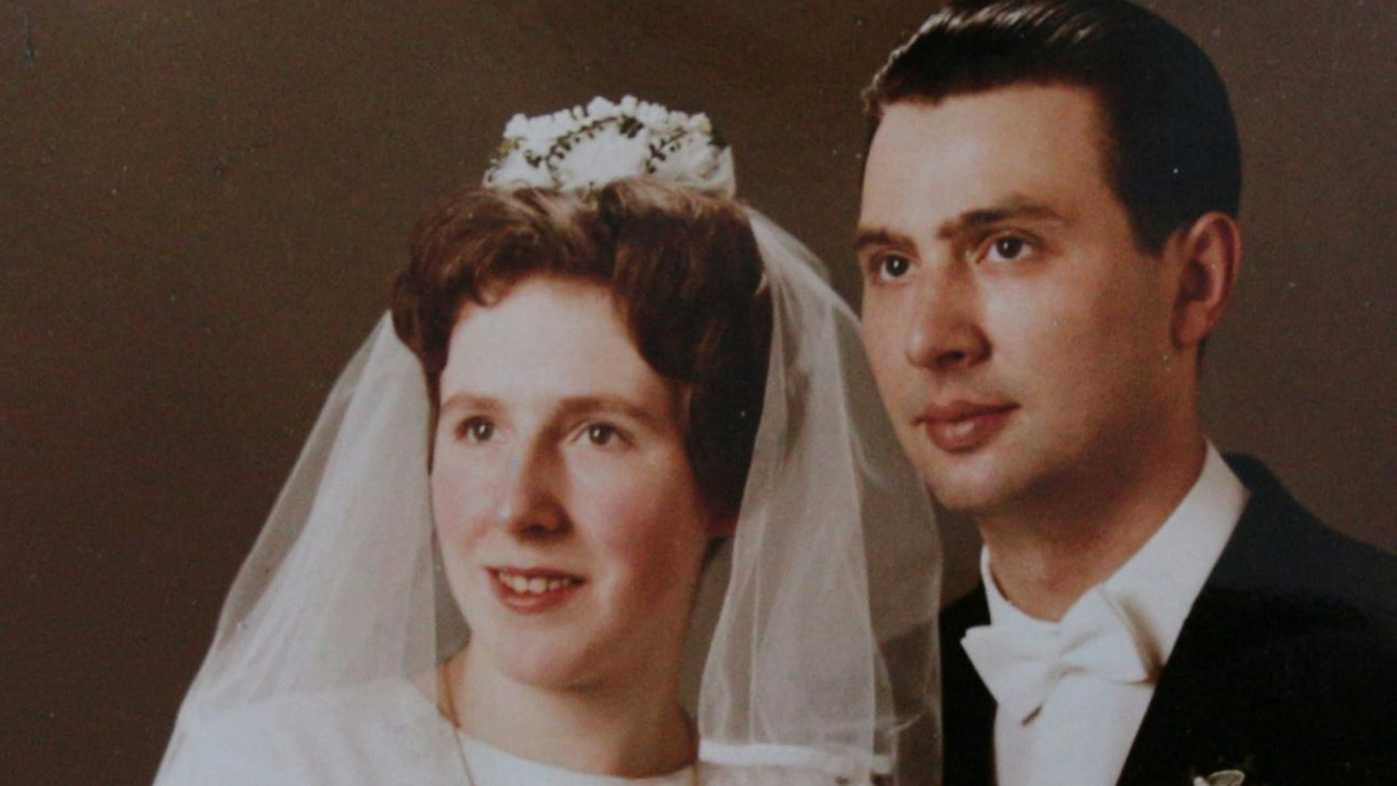 Aufnahme des Paars während seiner Hochzeit. Beide blicken lächelnd in die Ferne.