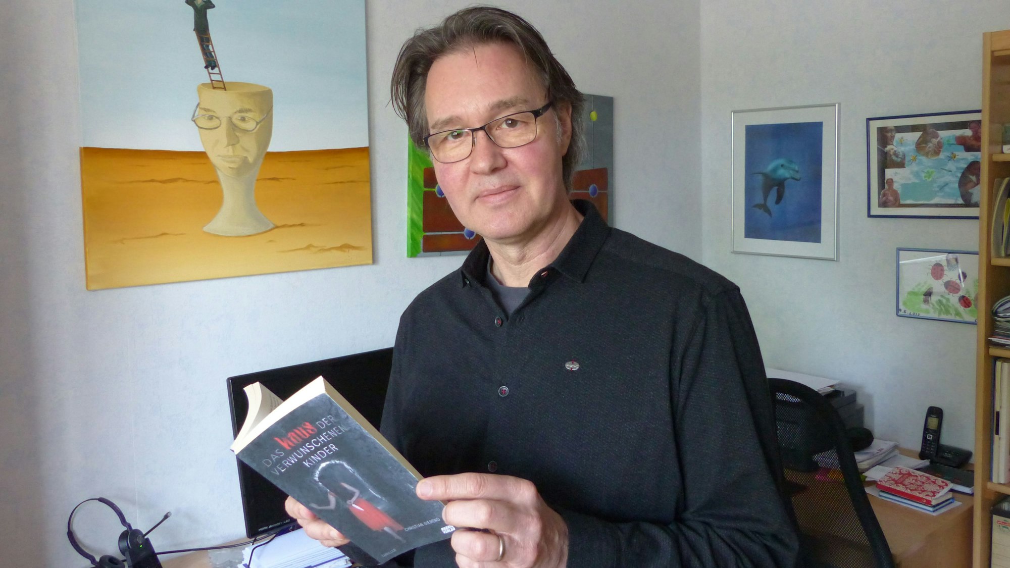 Christian Gierend steht in seinem Arbeitszimmer und blickt in die Kamera. Er hält sein Buch aufgeschlagen in den Händen.